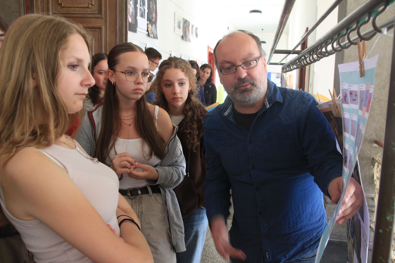 Im Schulflur: Robert Lorenz zeigt drei Schülerinnen ein Blatt, im Hintergrund weitere Personen,