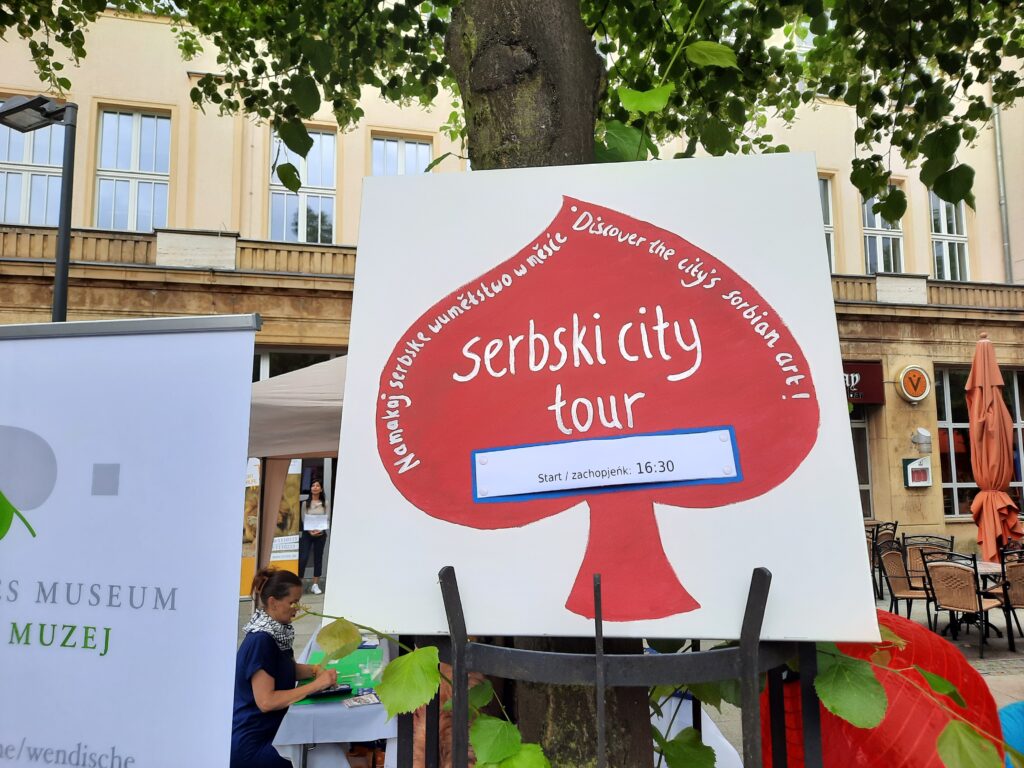 Hinweisschild mit Schriftzug "serbski city tour. namakaj serbske wuměłstwo w měsće. Discover the city's sorbian art!"